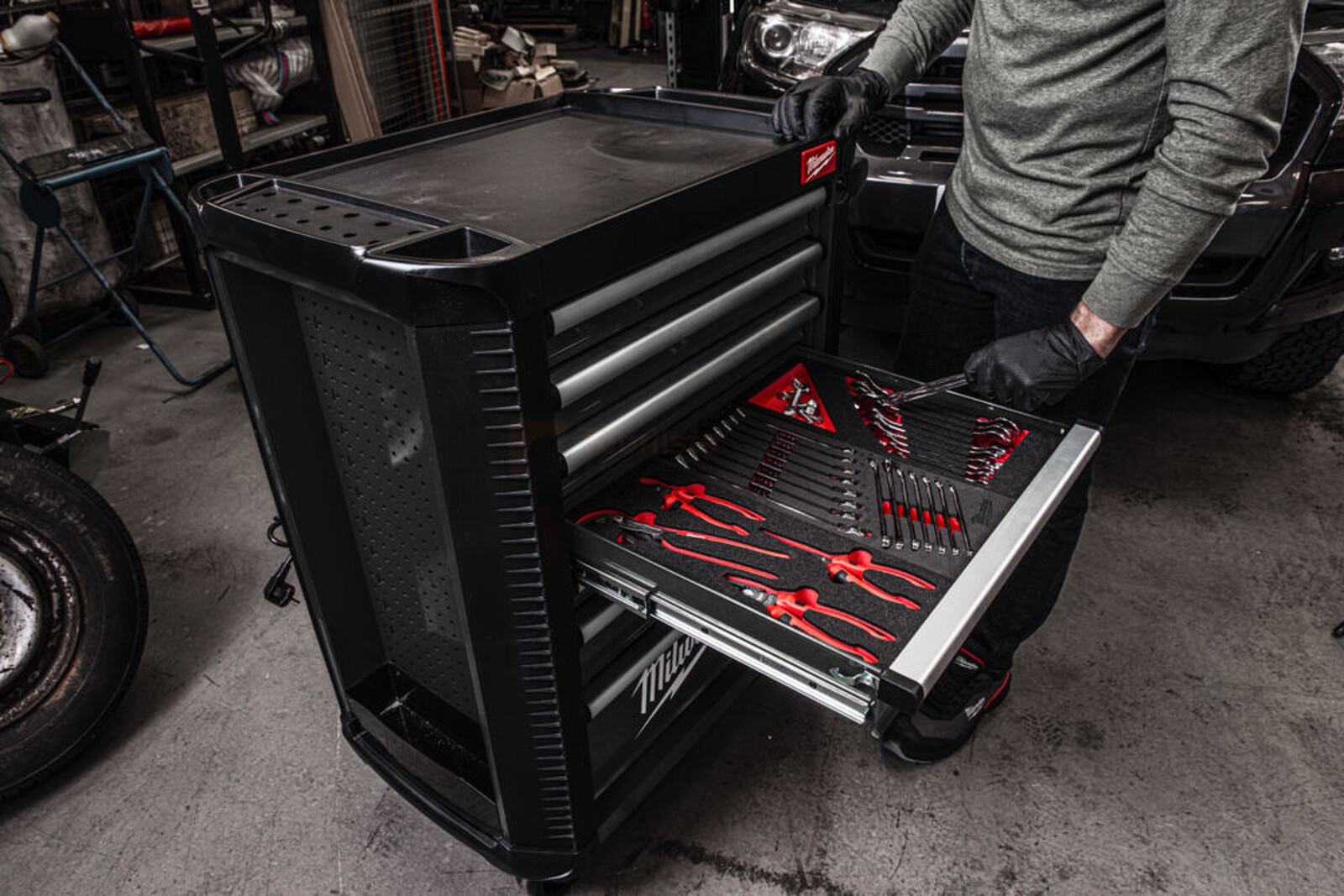 Pildil on mees, kes avab Milwaukee 206-osalise tööriistakomplekti sahtlit halli tööriistakäruga, mis on täis punaseid...