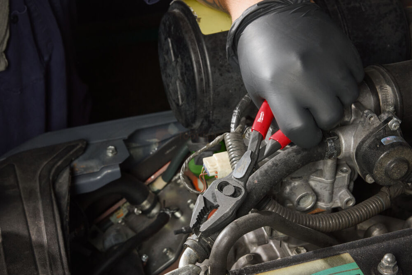 Pildil on näha, kuidas mehaanik kasutab Milwaukee 200 mm näpitsaid auto mootori kallal töötades.