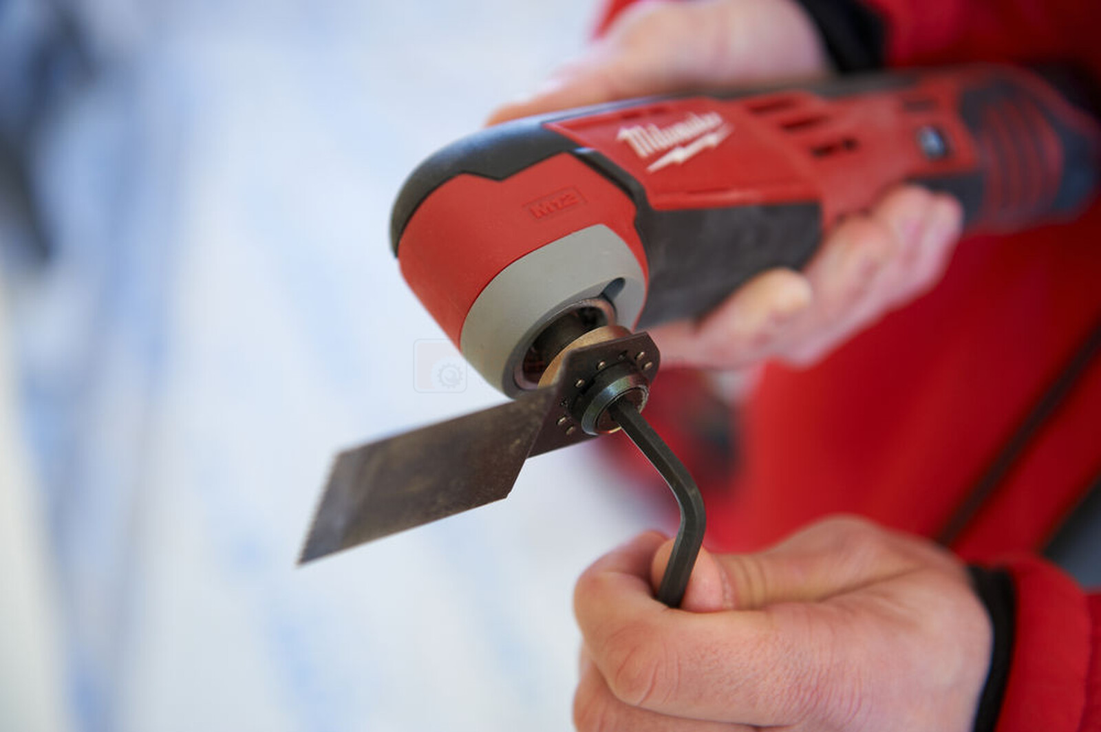 Pildil on näha, kuidas inimene vahetab Milwaukee akuuniversaaltööriista C12 MT-0 külge kinnitatud tera.