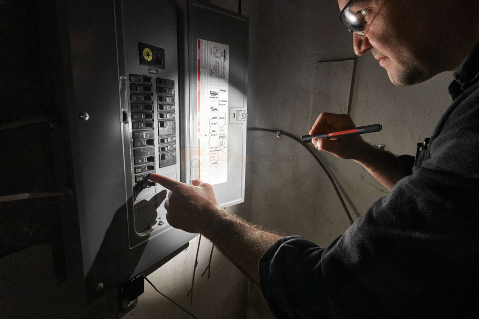 Pildil kasutab elektrik Milwaukee pliiatslampi ja pealampi, et valgustada elektrikilpi ja kontrollida kaableid.