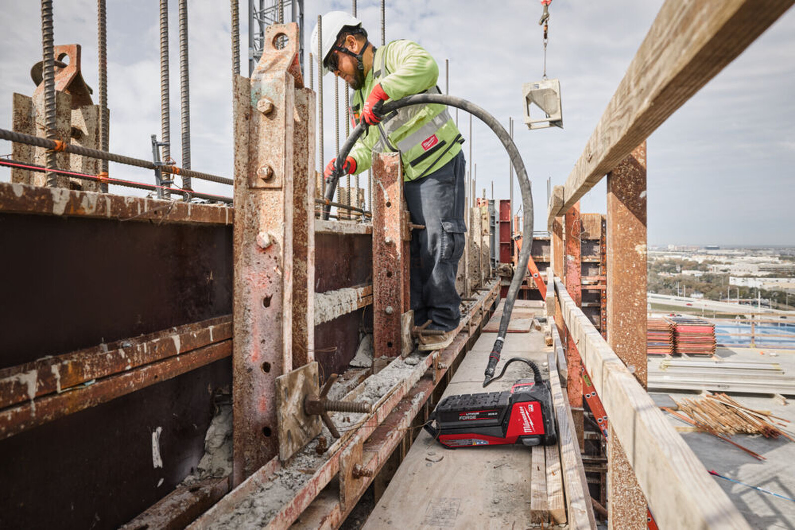 Pildil on ehitustöölise kasutuses Milwaukee akubetoonivibraator, mis on ühendatud voolikuga, tõenäoliselt tolmu...