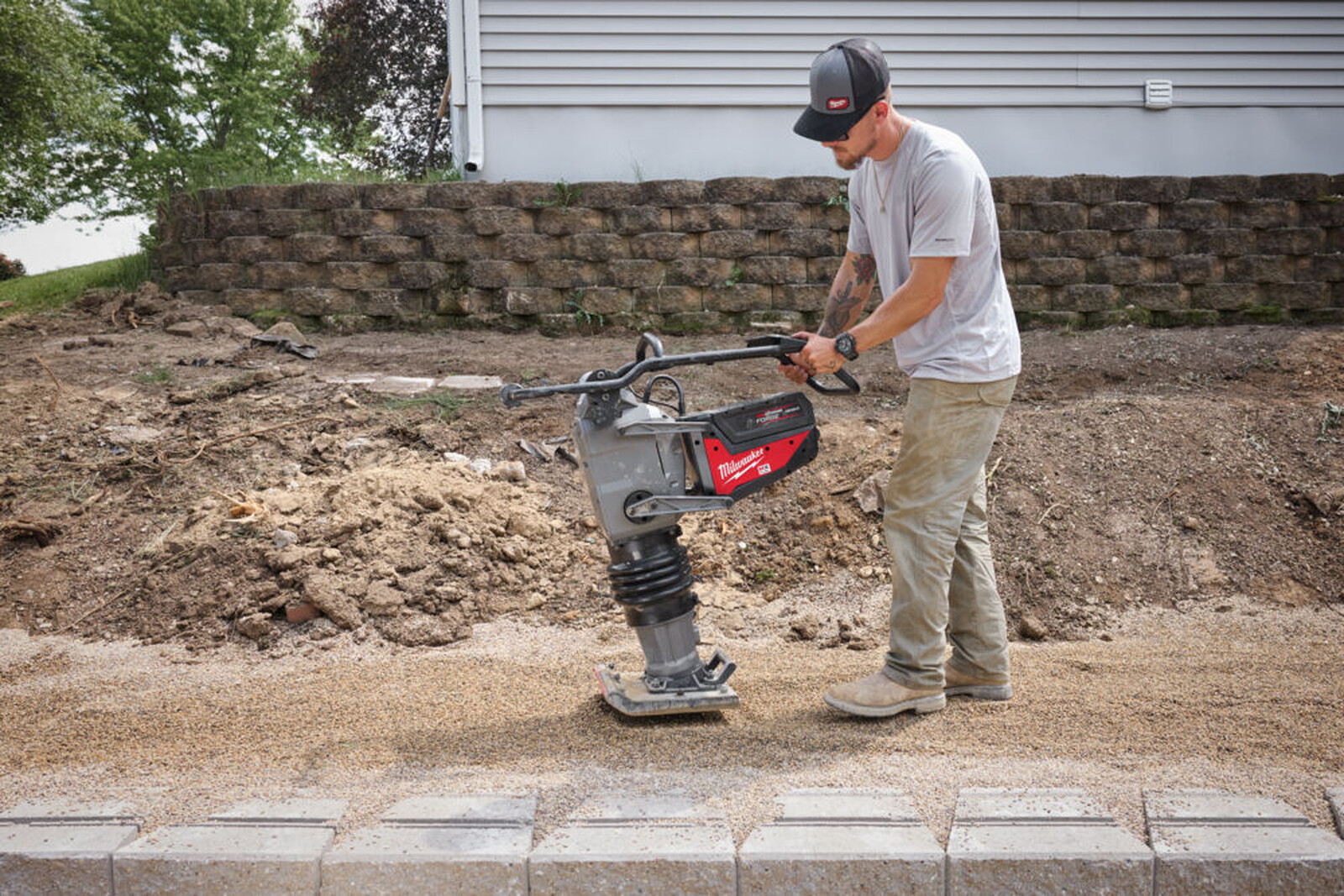 Pildil on mees, kes kasutab Milwaukee akutoitel vibroplaati MXF RAM60-0, tihendades pinnast ehitusplatsil.