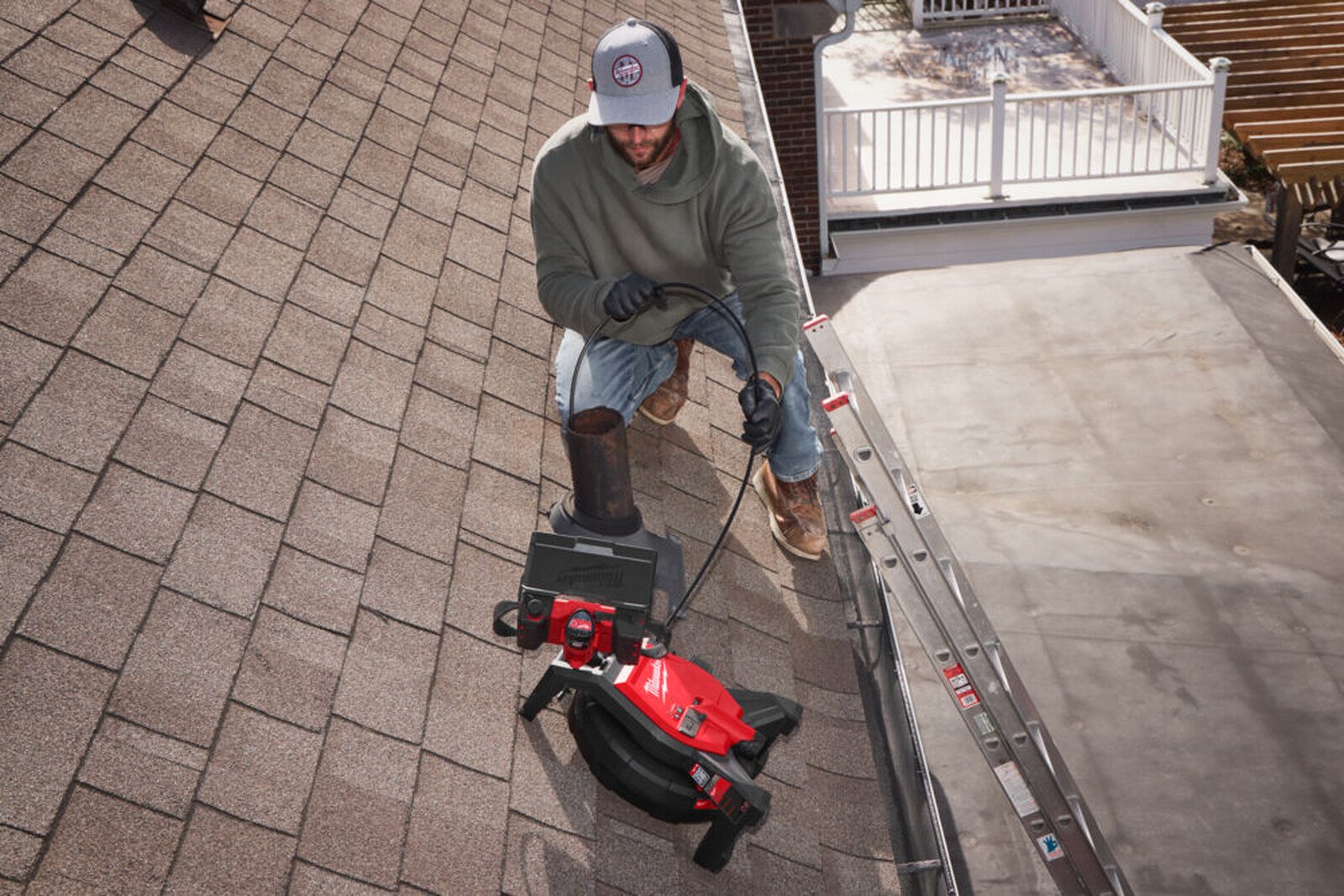 Pildil on mees, kes kasutab Milwaukee kontrollkaamerat M12 SICO26-0 katuse peal, et kontrollida korstnat.