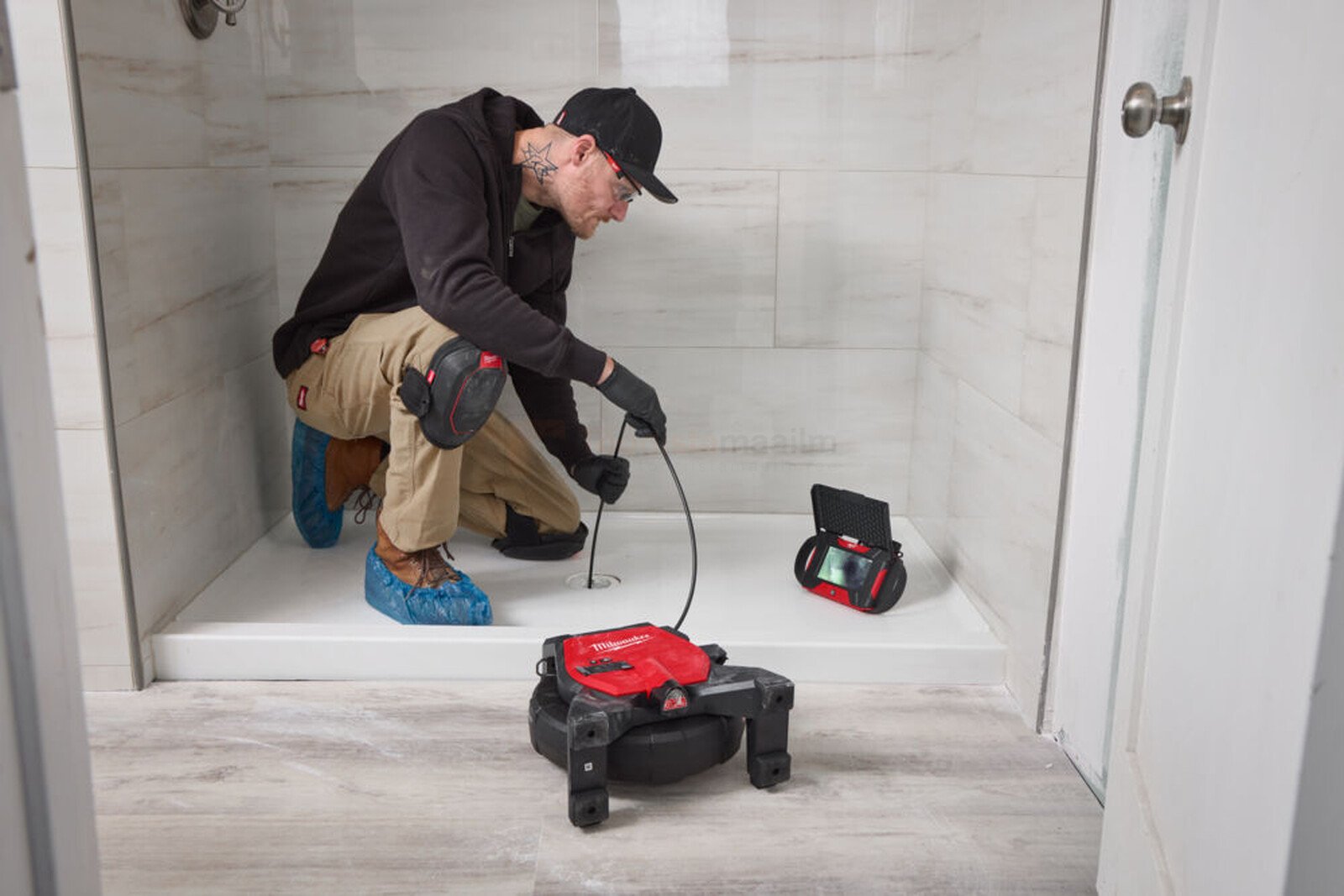 Pildil on mees, kes kasutab Milwaukee kontrollkaamerat M12 SICO20-0, et uurida duširuumi äravoolu.