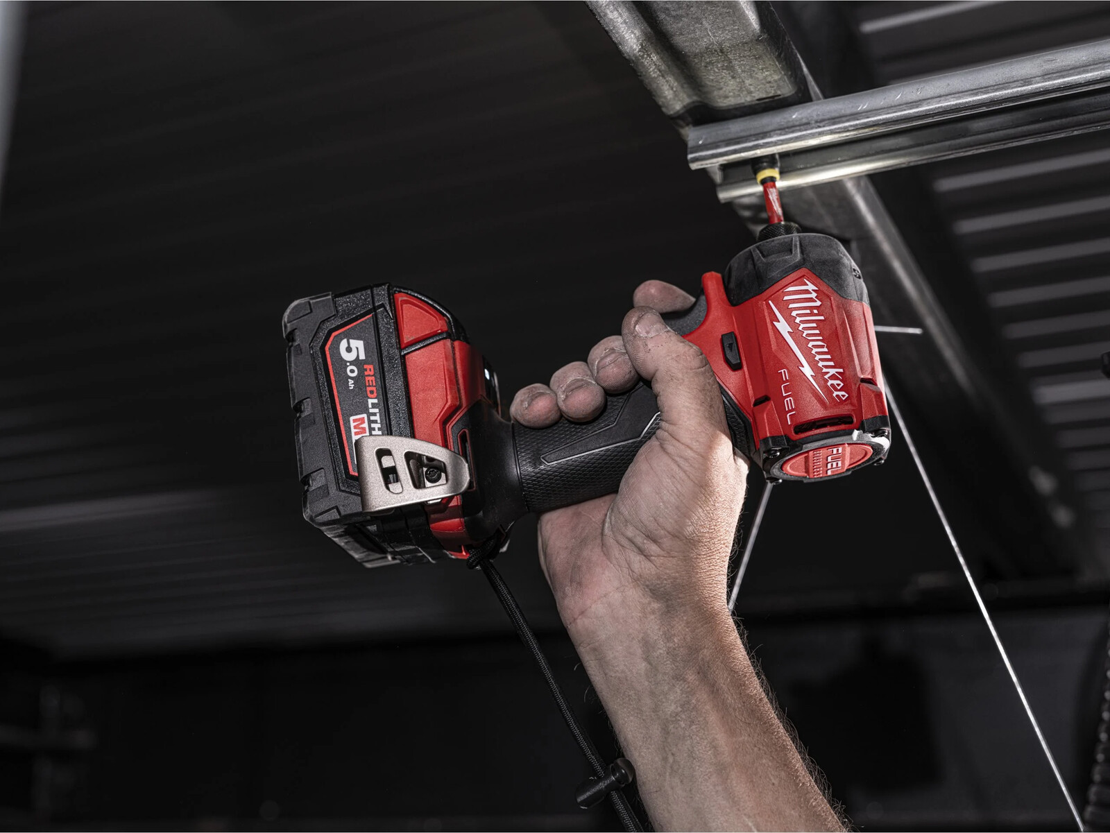 Pildil on näha, kuidas inimene kasutab Milwaukee M18 FIDRQ-0X hüdraulilist akulöökkruvikeerajat, mis on kinnitatud lae külge.