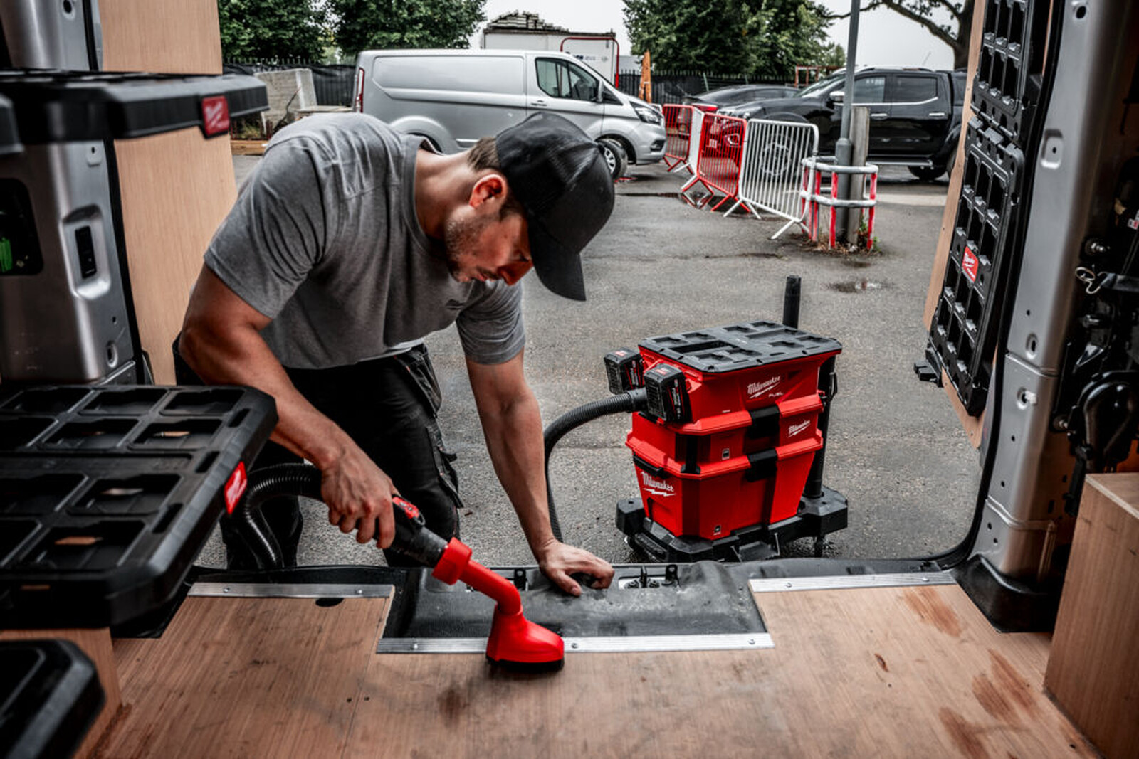 Pildil on mees, kes kasutab Milwaukee akuga vee- ja tolmuimejat, et puhastada kaubiku põrandat.