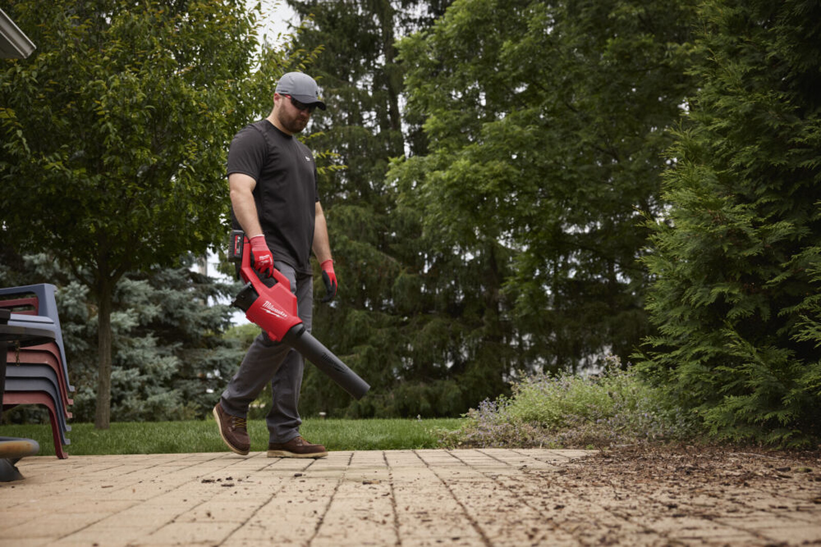 Pildil on mees, kes kasutab Milwaukee akutoitega lehepuhurit, et puhastada lehti ja prahti terrassilt.