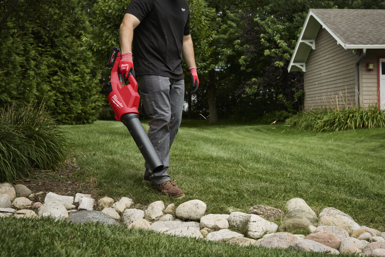 Pildil on mees, kes kasutab Milwaukee akutoitega lehepuhurit, et puhastada rohtu ja kive.