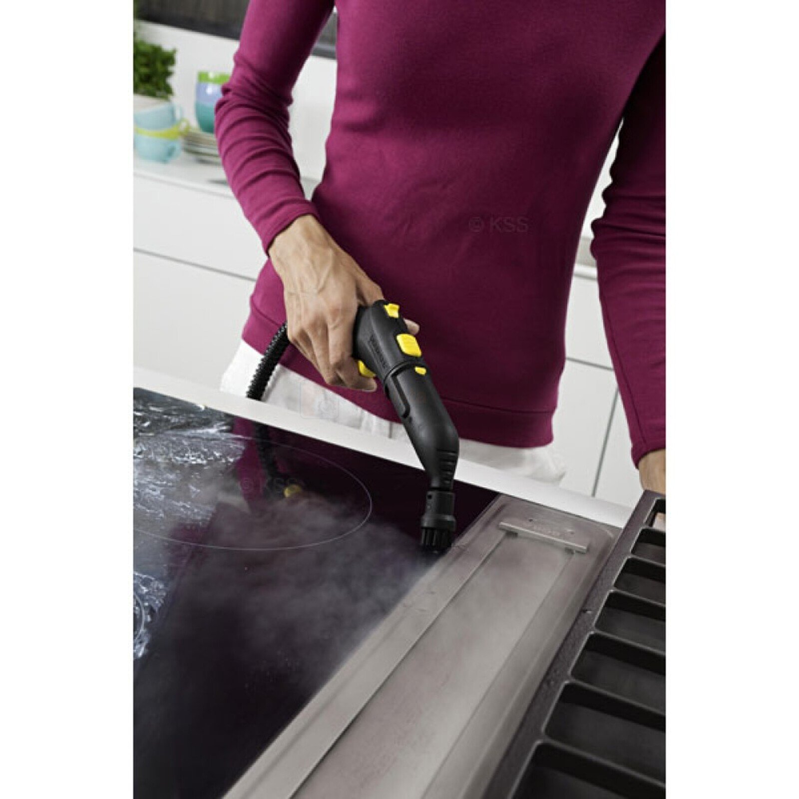 Pildil on naine, kes puhastab Kärcheri punktotsikuga aurupesurit pliidiplaati.