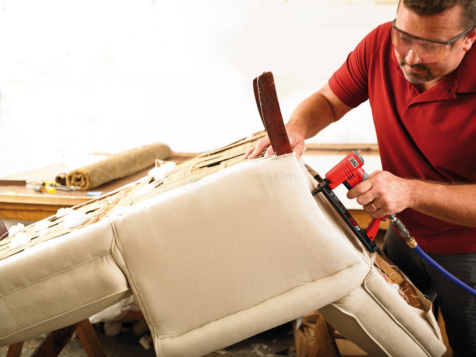 Pildil on mees, kes kasutab SENCO klambripüstolit SFW09-C mööbli restaureerimisel, kinnitades kangaid diivani külge.