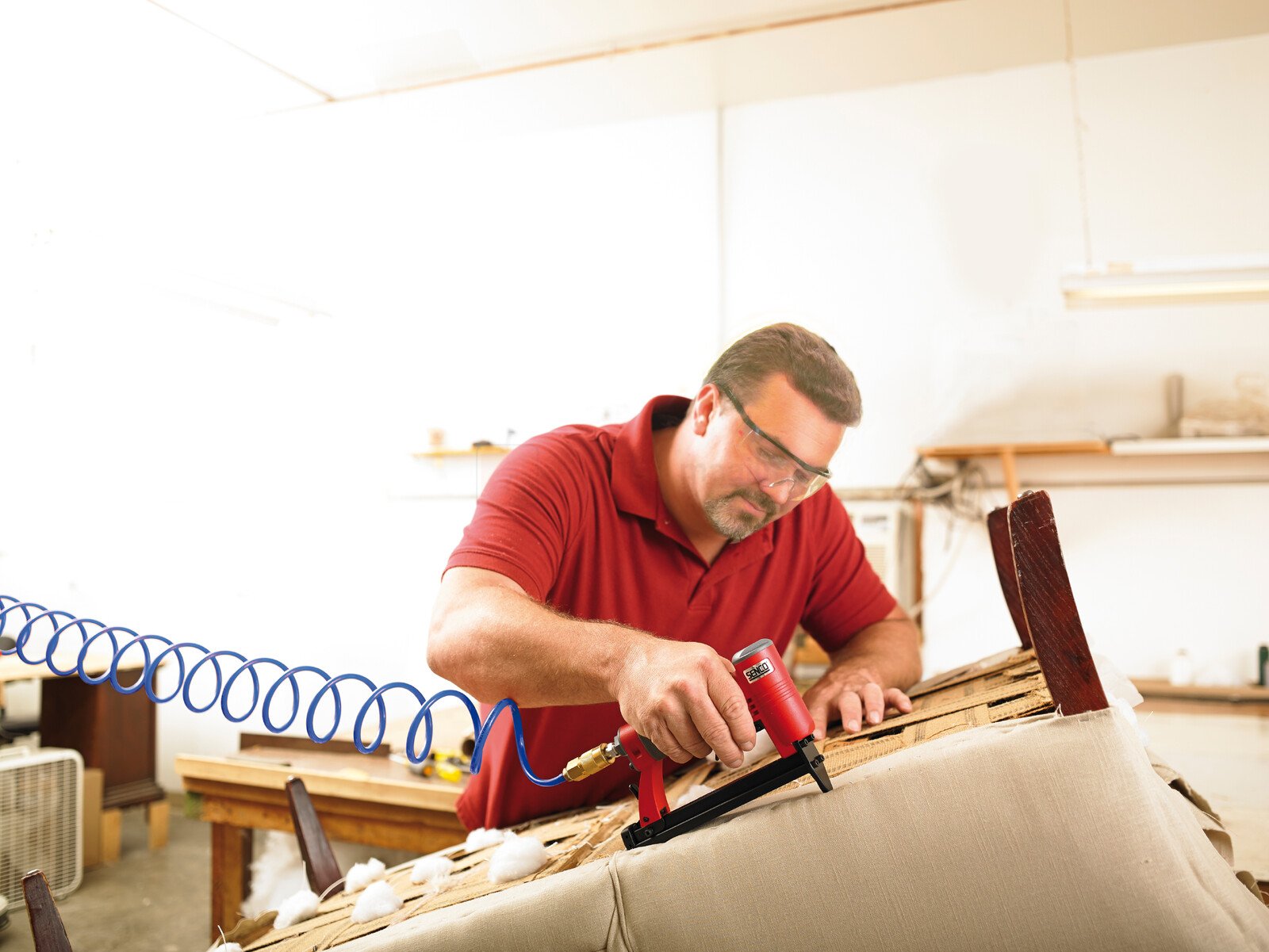 Pildil on mees, kes kasutab SENCO klambripüstolit SFW09-C, et kinnitada materjali mööblile.