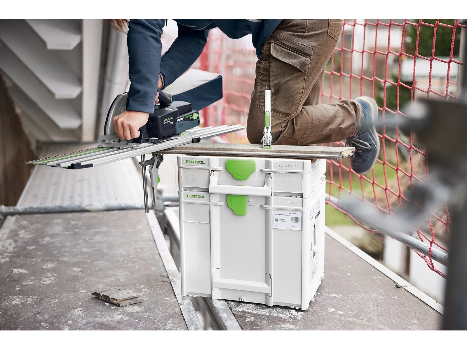 Pildil on ehitaja, kes kasutab Festool mobiilset tööpinki-Systainer³ SYS3-MFT M 112, et saagida puitu, samal ajal kui...