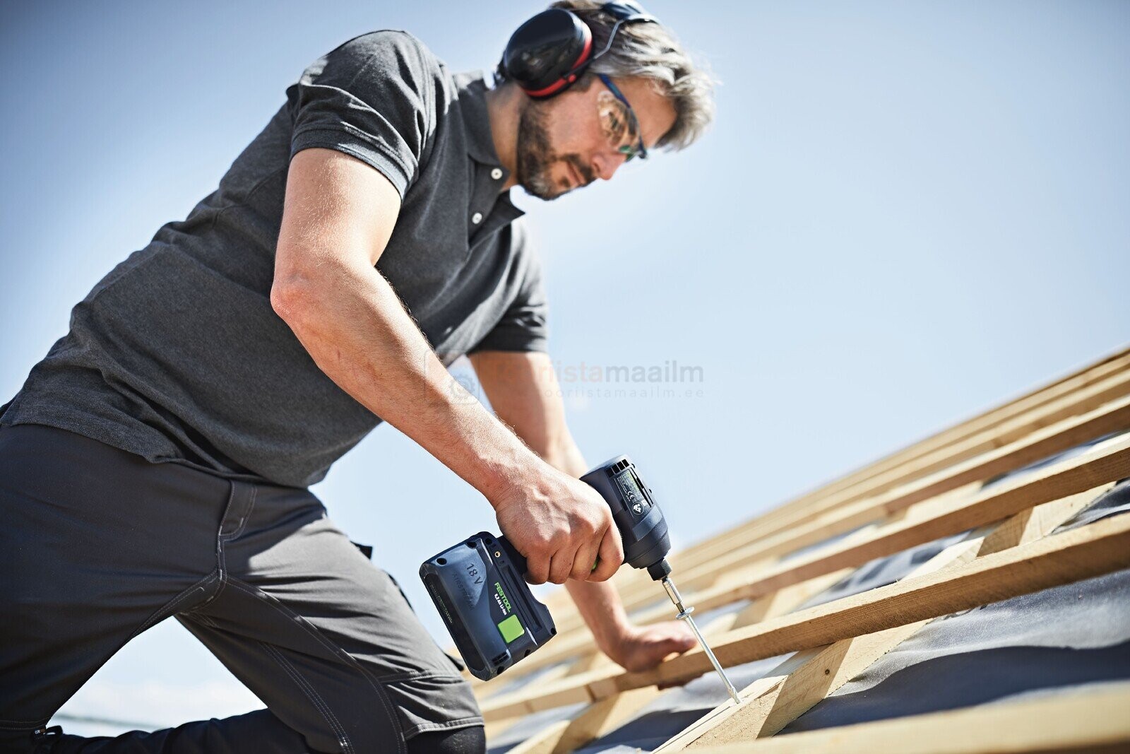 Pildil on mees, kes kasutab Festool akutööriistade komplekti TID 18 Basic-Set T18, et kruvida puitkonstruktsiooni, kandes...