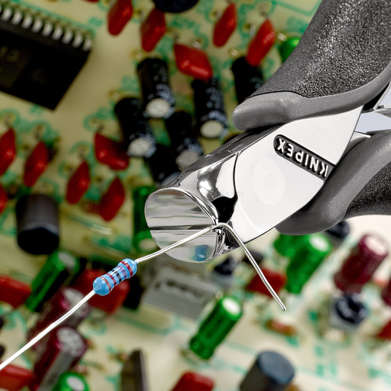 Pildil on näha, kuidas Knipex ESD lõikekäärid lõikavad elektroonilise komponendi jalga, taustal on trükkplaat ja...