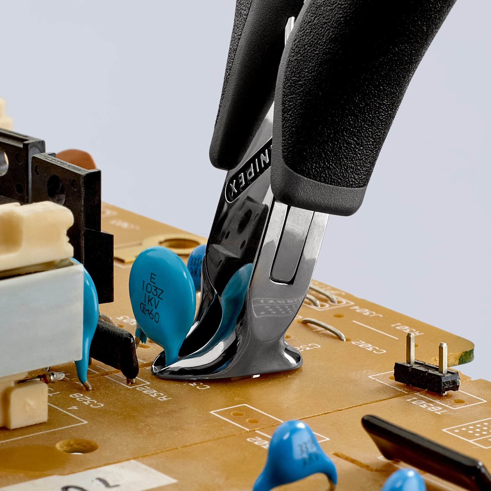 Pildil on näha musta kindaga käsi, mis kasutab Knipex ESD lõikekäärid 120mm elektroonikaplaadil komponentide lõikamiseks.