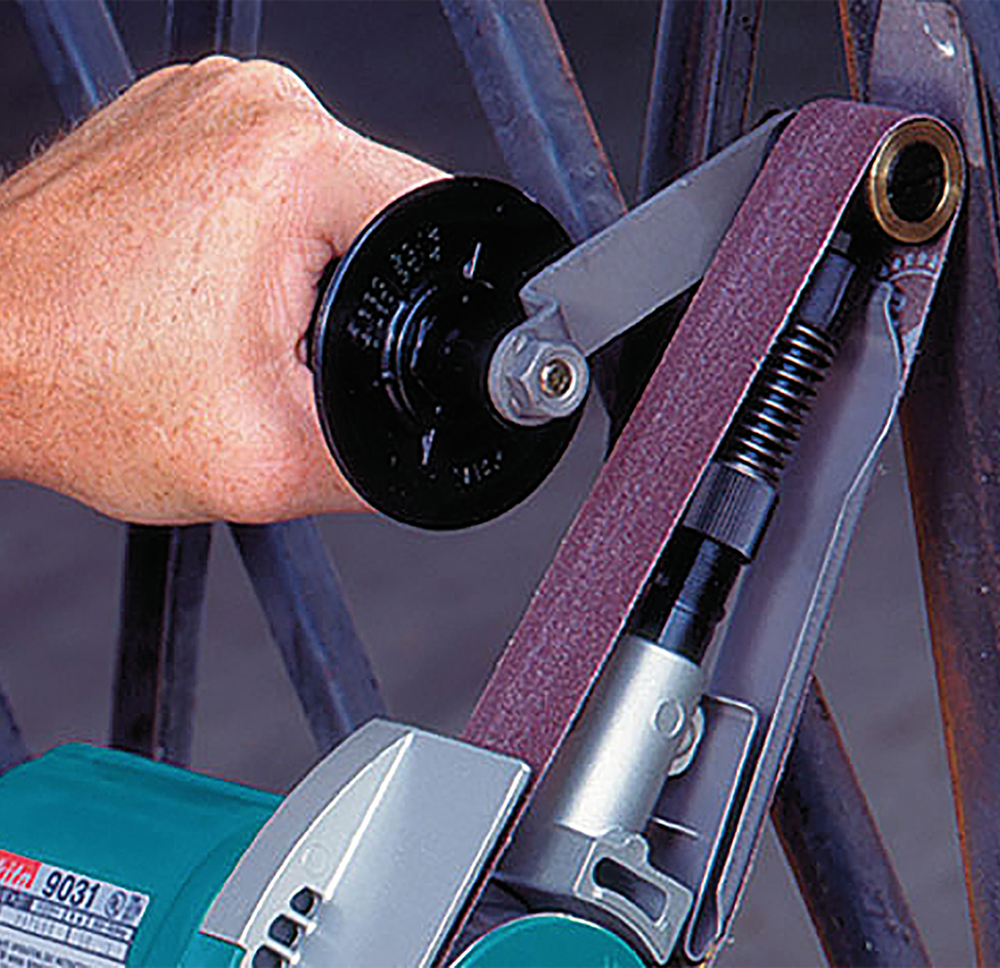 Pildil on detailivaade Makita lintlihvmasinast 9031, mida hoiab käes inimene, näha on lihvimislint ja masina ehitus.