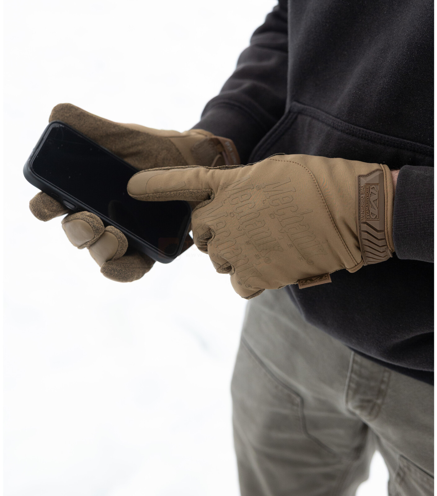 Pildil on inimene, kes kannab Mechanix Wear ColdWork Original Coyote talviseid kindaid ja kasutab telefoni.