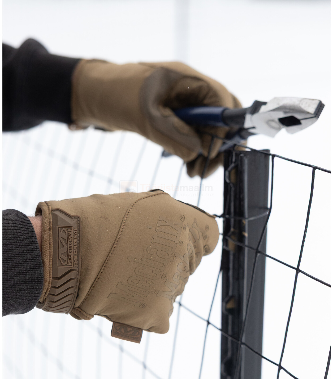 Pildil on näha, kuidas isik kasutab MECHANIX WEAR ColdWork Original Coyote talviseid kindaid, et parandada aeda...