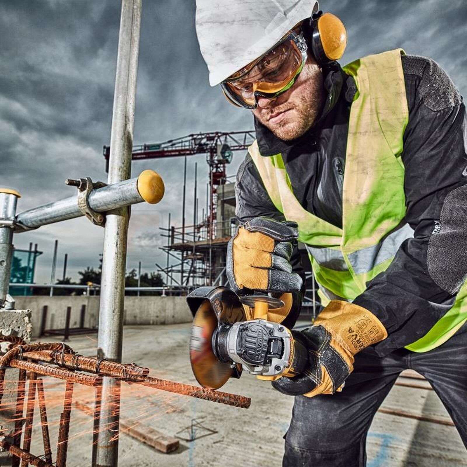 Pildil on ehitustöötaja, kes kasutab DeWalt nurklihvijat, et lõigata metalli, samal ajal kui ta kannab kaitsevarustust.