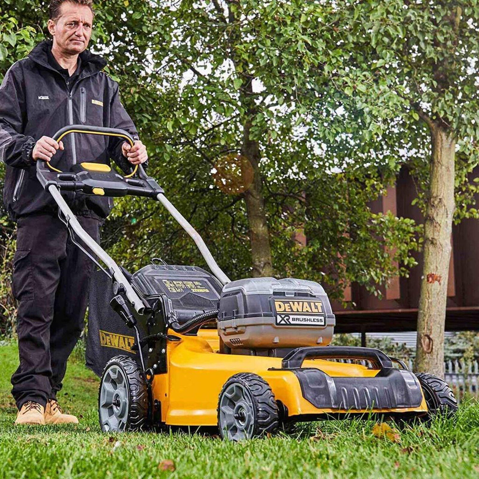 Pildil on mees, kes lükkab rohelisel murul kollast DeWalt akumuruniidukit DCMW564P2.