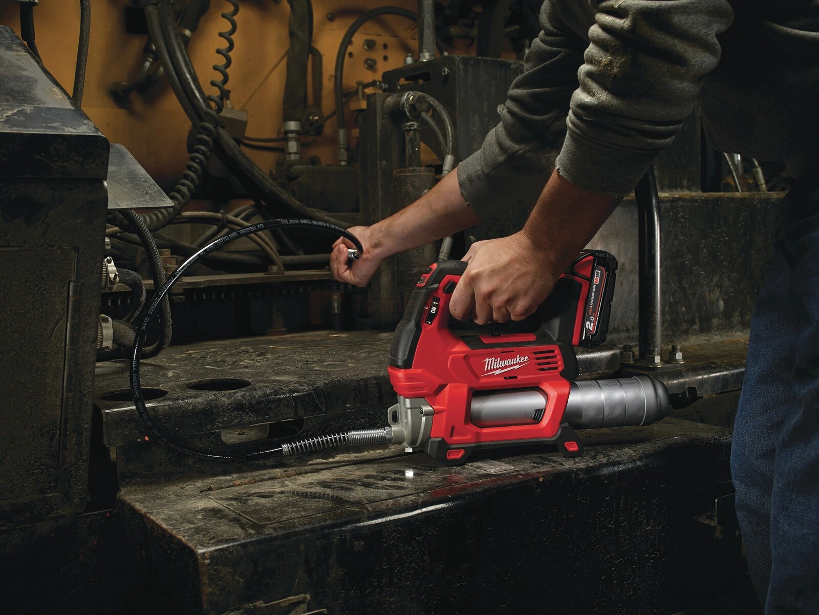 Pildil on mees, kes kasutab Milwaukee M18 POWERPACK M18 FPP3AK-523B akutoitega määrdepritsi, et määrida masinat.