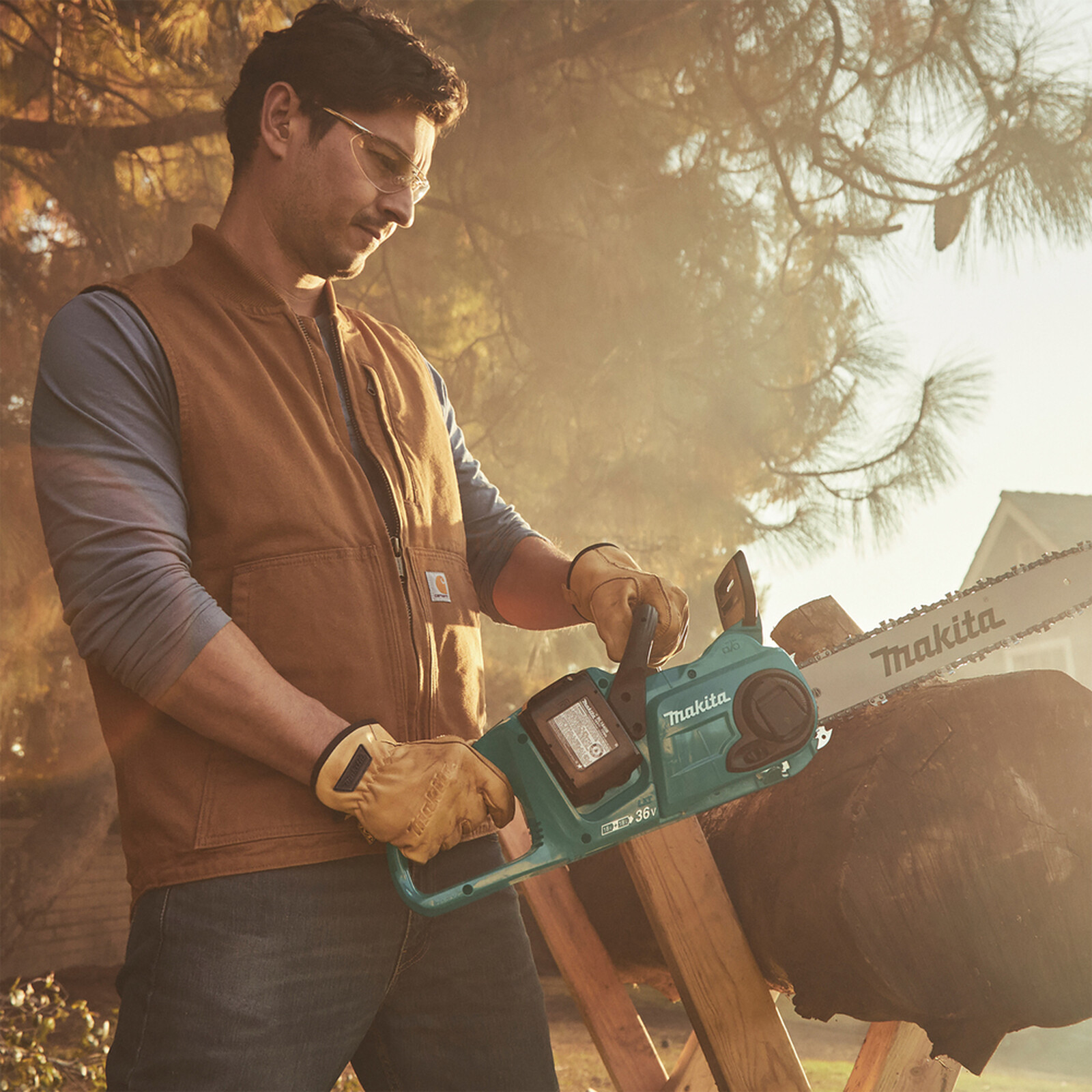 Pildil on mees, kes kannab Makita nahast töökindaid ja kasutab Makita mootorsaagi puidu lõikamiseks.