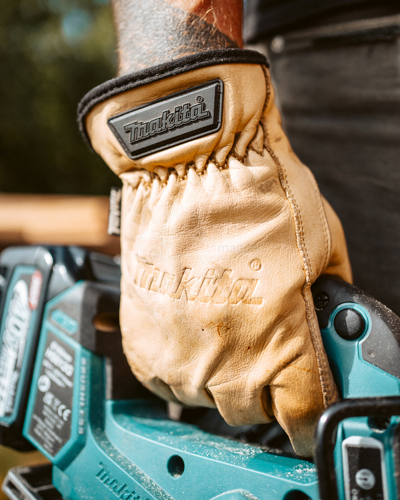 Pildil on mees, kes kannab Makita nahast töökindaid, hoides samal ajal Makita tööriista.