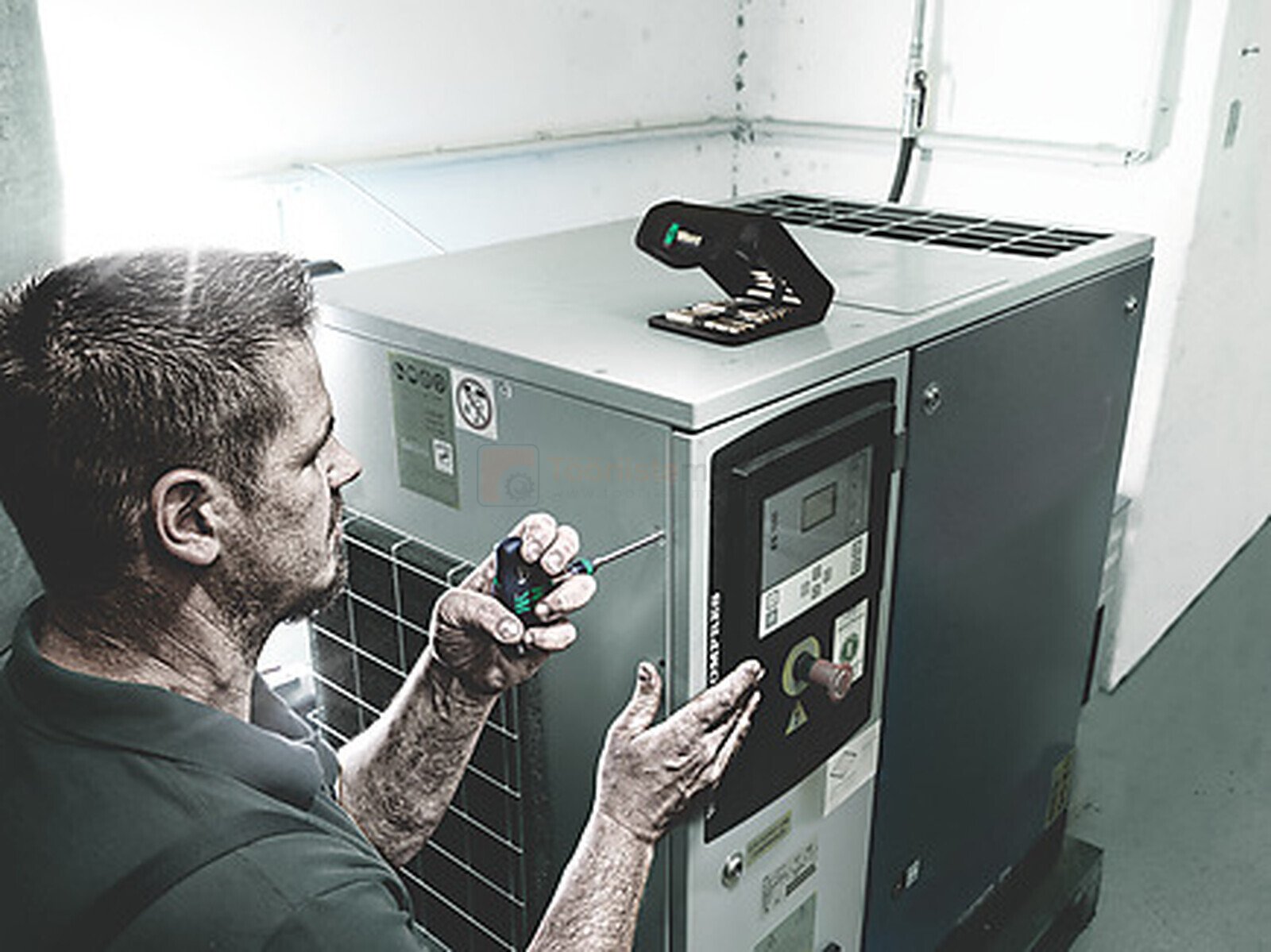 Pildil on mehaanik, kes kasutab Wera Kraftform Kompakt 62 otsakkruvitsa komplekti, et parandada suurt tööstuslikku seadet.