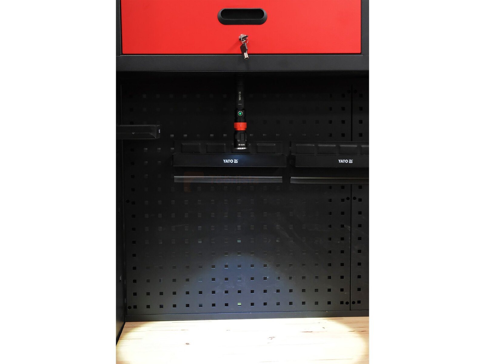 Pildil on näha YATO LED töövalgusti, mis on kinnitatud musta värvi tööriistaseina külge, mille kohal on punane sahtel.