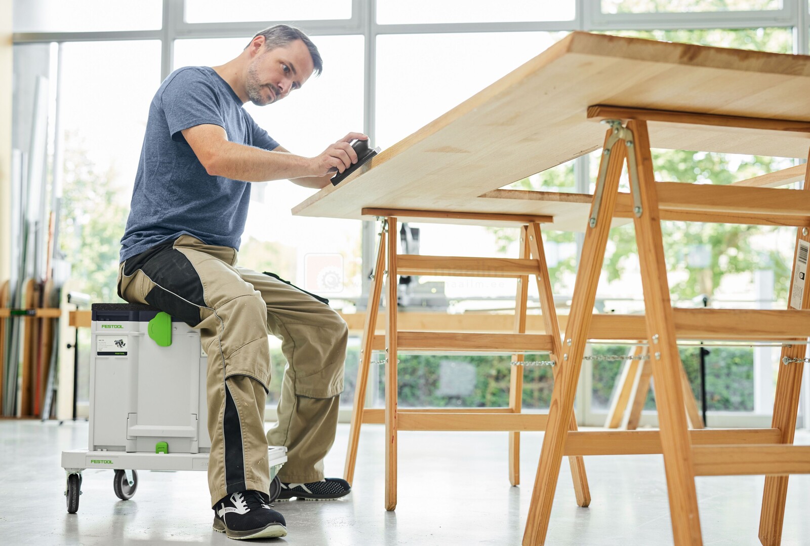 Pildil istub mees Festool istmepadjaga SK-CT/SYS varustatud tööriistakastil, hööveldades suurt puidutahvlit.