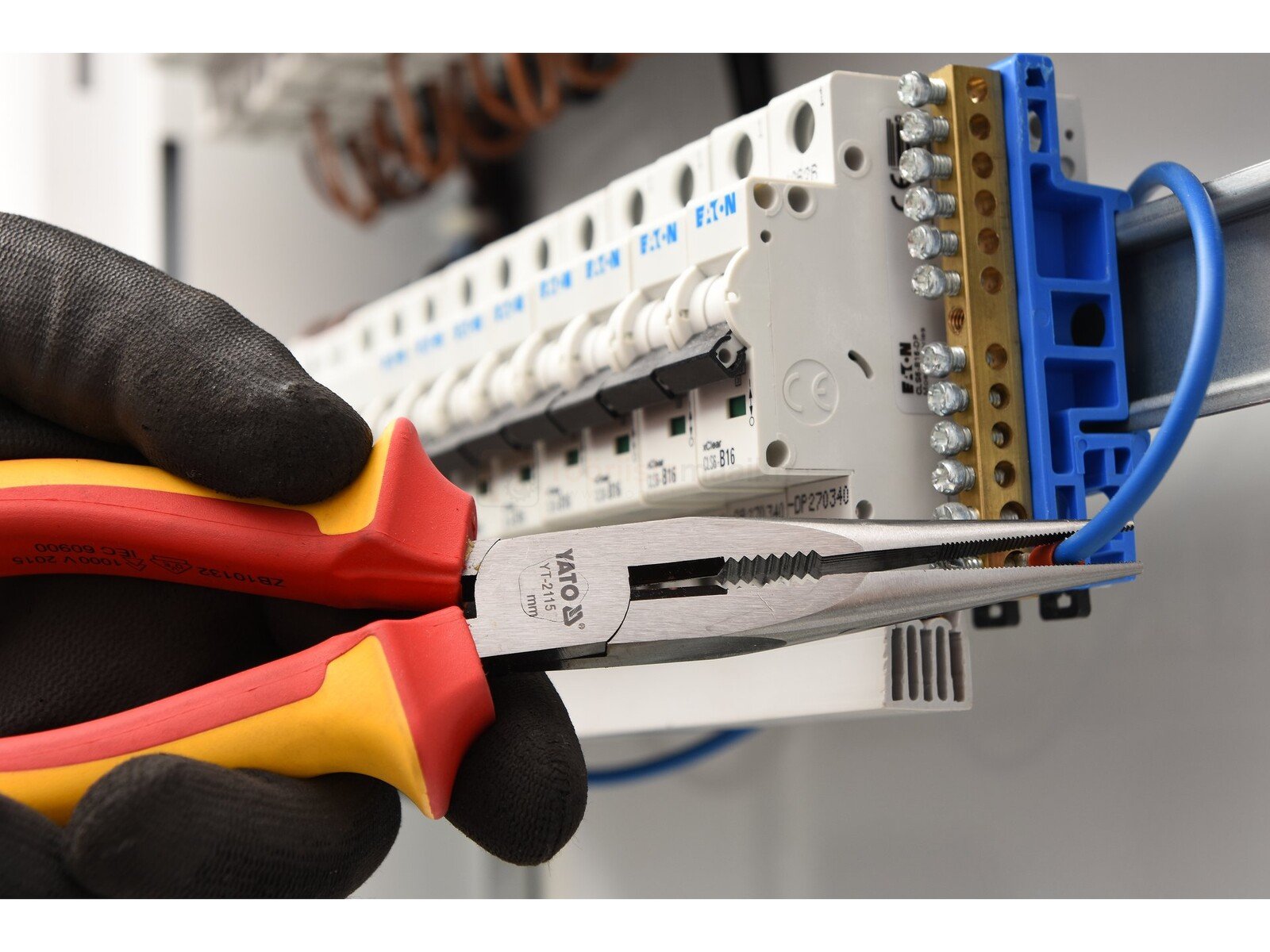Pildil on näha mustade kinnastega käsi, mis kasutab YATO VDE pikkmokktange 160 mm, et töötada elektrisüsteemiga.