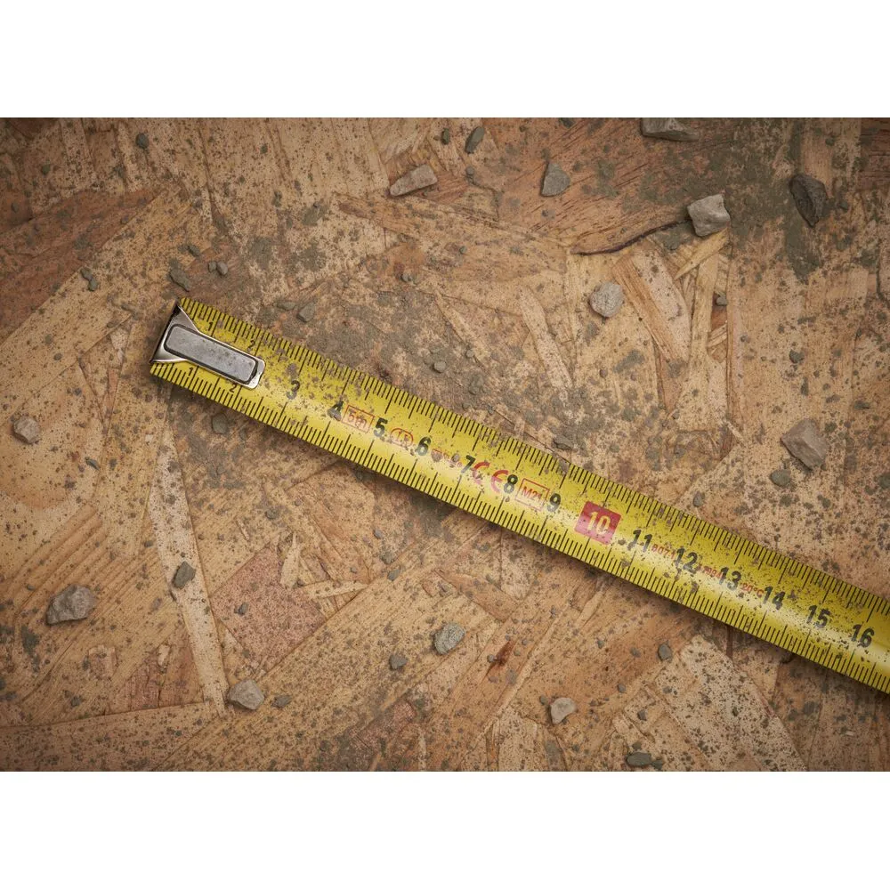 Pildil on määrdunud puitpõrandal Stanley PowerLock 5 m x 19 mm mõõdulint, millel on näiduava, lisaks näeme väikseid kive...