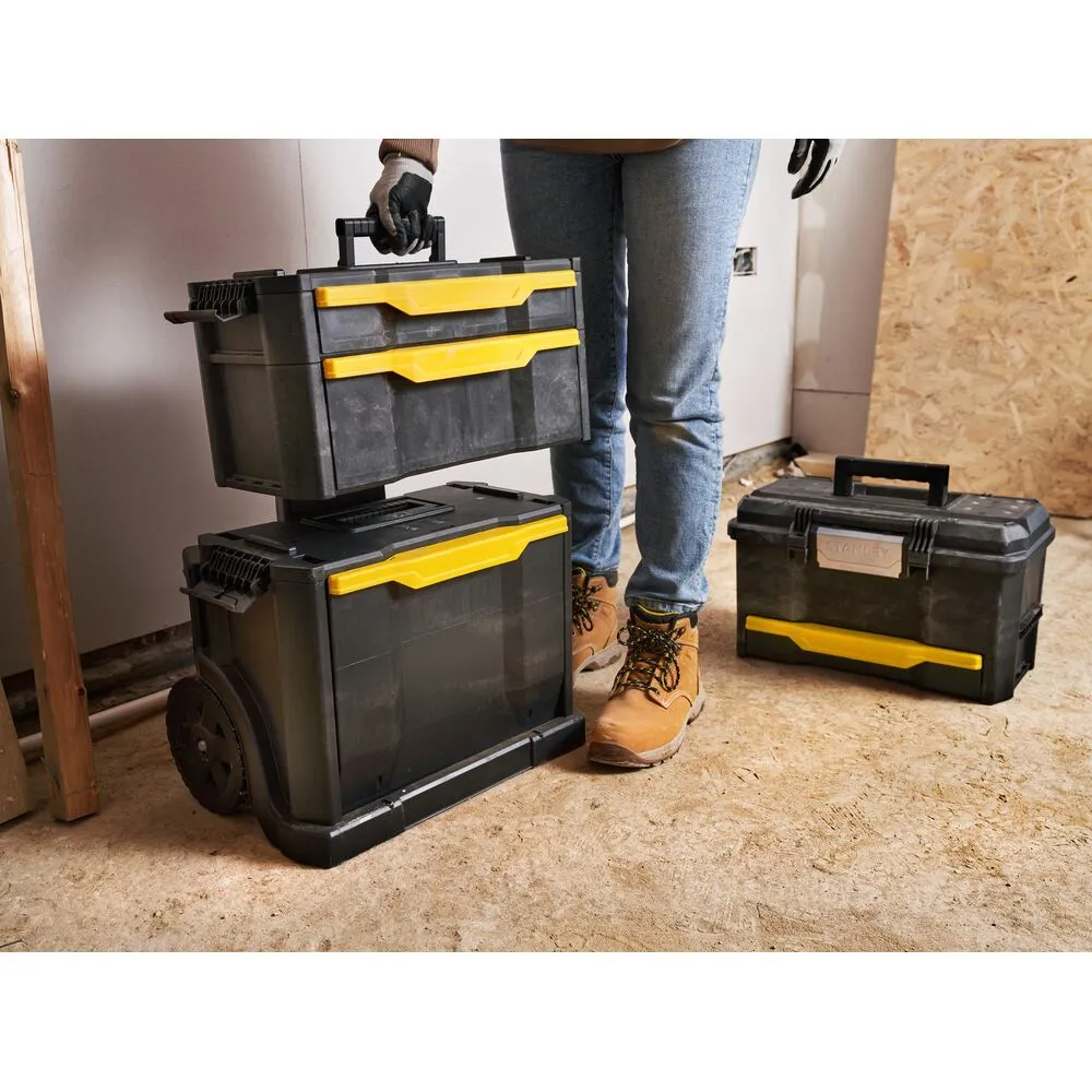 Pildil on näha Stanley tööriistakast ratastel 3in1, mida hoiab inimene ja see on osaliselt lahti, et näidata selle sahtleid.