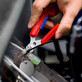 Pildil on käsi, mis kasutab Knipex külglõiketange Slim 150 mm koos hoidikuga, et lõigata kaablisidet.