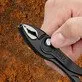 Pildil on käsi, mis hoiab Knipex TwinGrip näpitsatange, mille lõuad on avatud ja nähtaval on roostes taust.