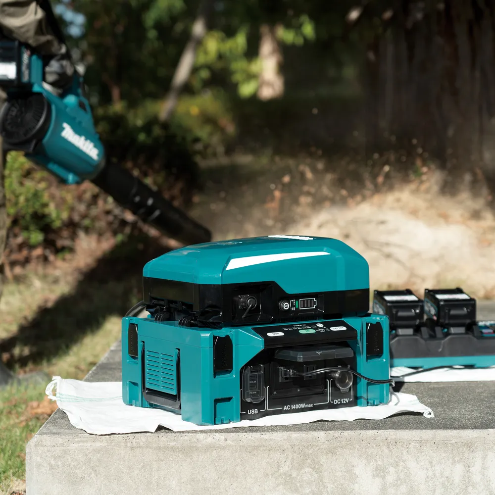 Pildil on näha Makita akuinverter BAC01 koos akude ja elektrilise puhuriga, mis on välitingimustes paigutatud.
