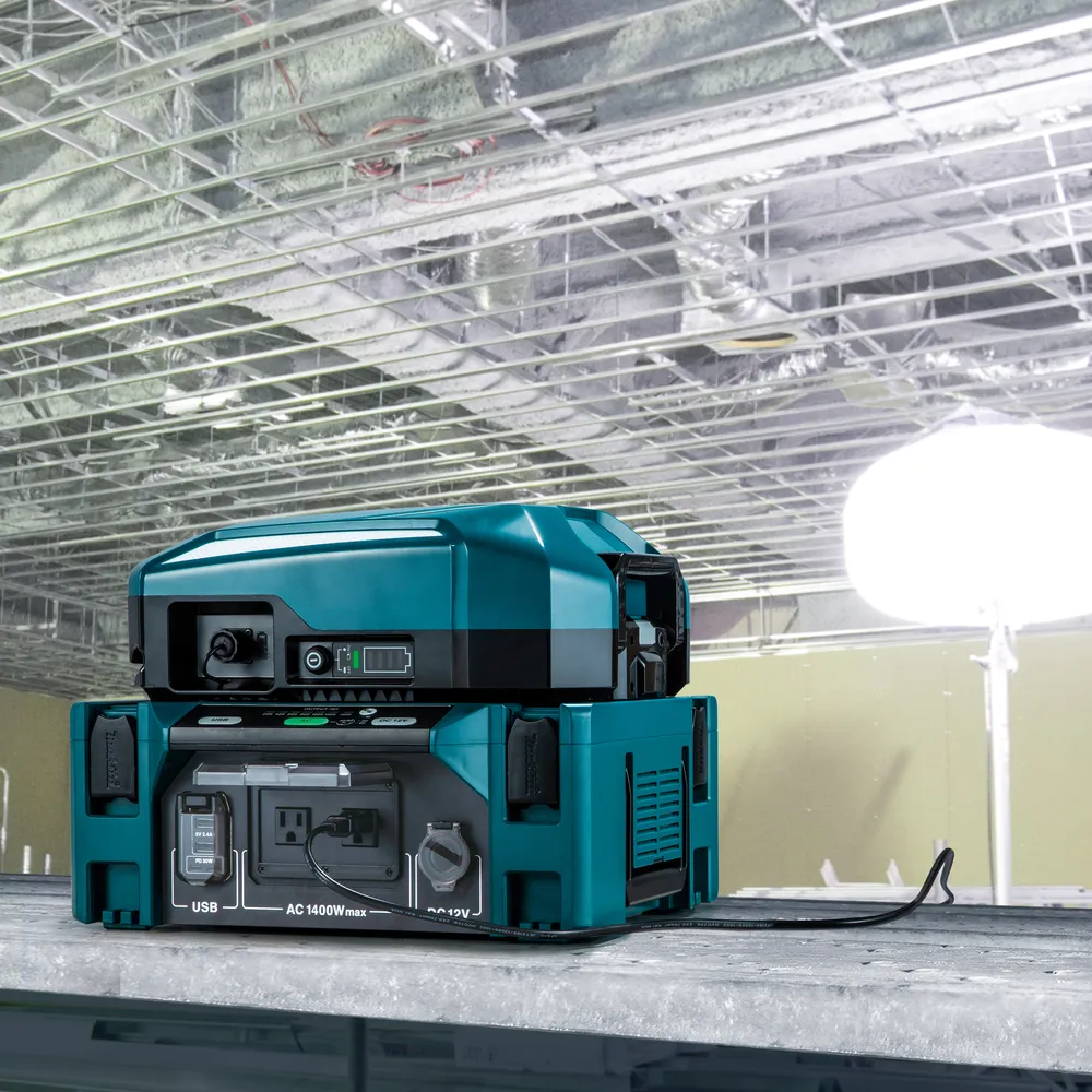 Pildil on Makita akuinverter BAC01, mis on asetatud töölaua peale laesüsteemiga ja valgustusega taustal.