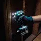 Pildil on Makita DLX2527TJ combokit, millega kruvitakse puidule kruvi, samal ajal kui tööriista valgustus valgustab...