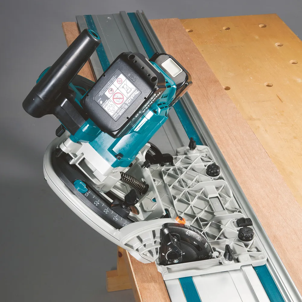 Pildil on Makita akuketassaag DSP601ZJU, mis on paigutatud koos juhikuga puidutöötlusalusele.