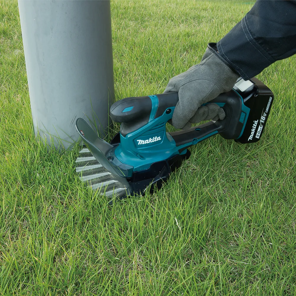 Pildil on Makita akuga murukäärid DUM604ZX, millega kärbitakse muru posti ümbert.