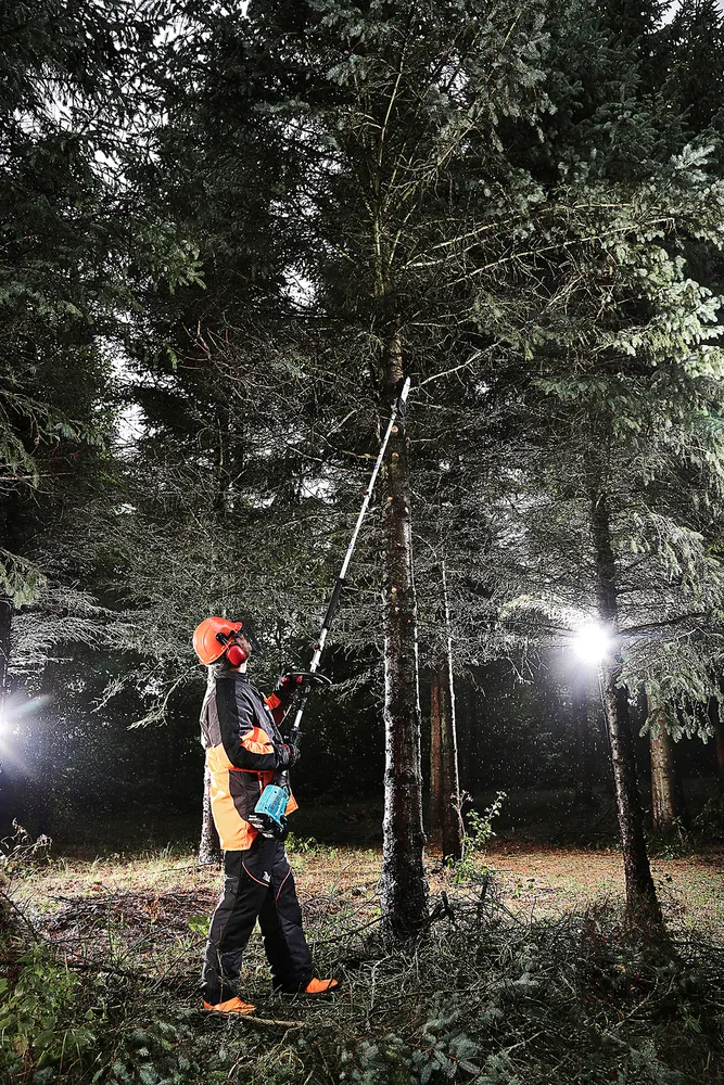 Pildil on näha mees, kes kasutab Makita vahetatavate tarvikutega akutrimmerit DUX60Z, et pügada puu oksi.