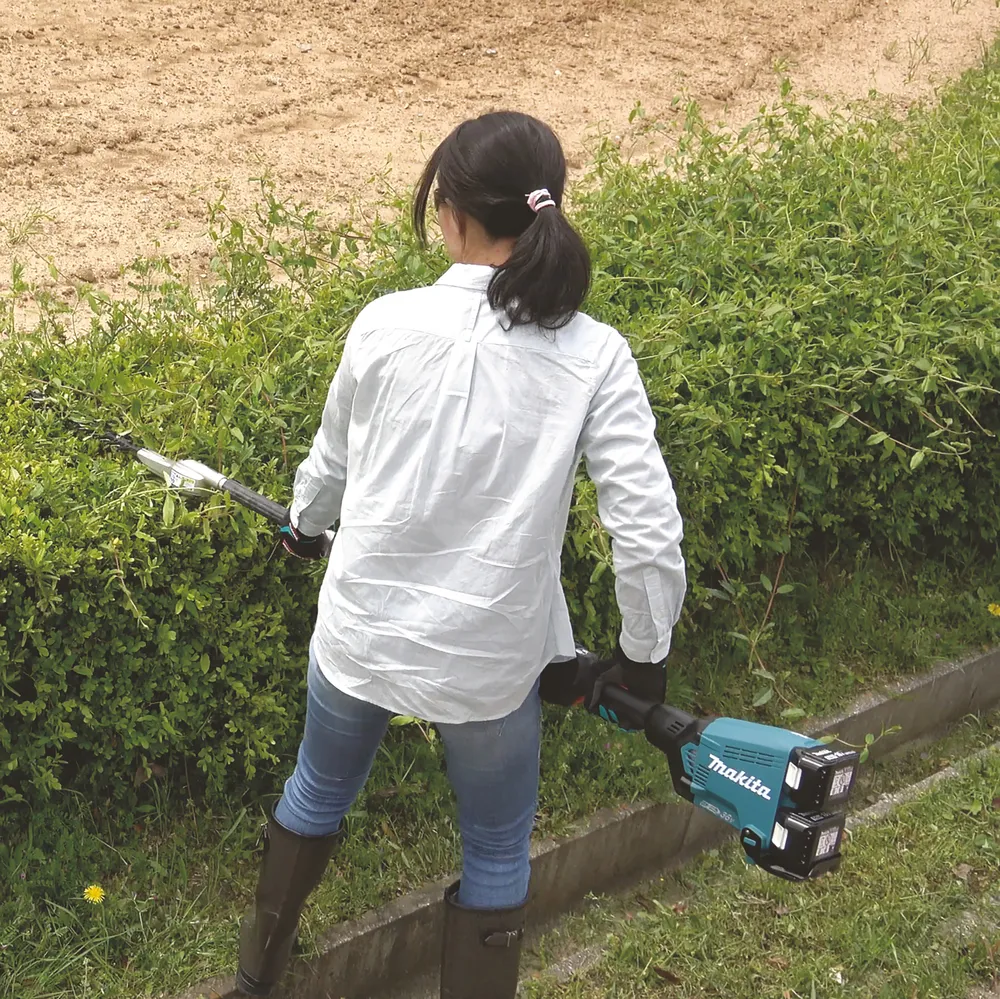 Pildil on Makita vahetatavate tarvikutega akutrimmer DUX60Z, mida kasutab naine heki pügamiseks.