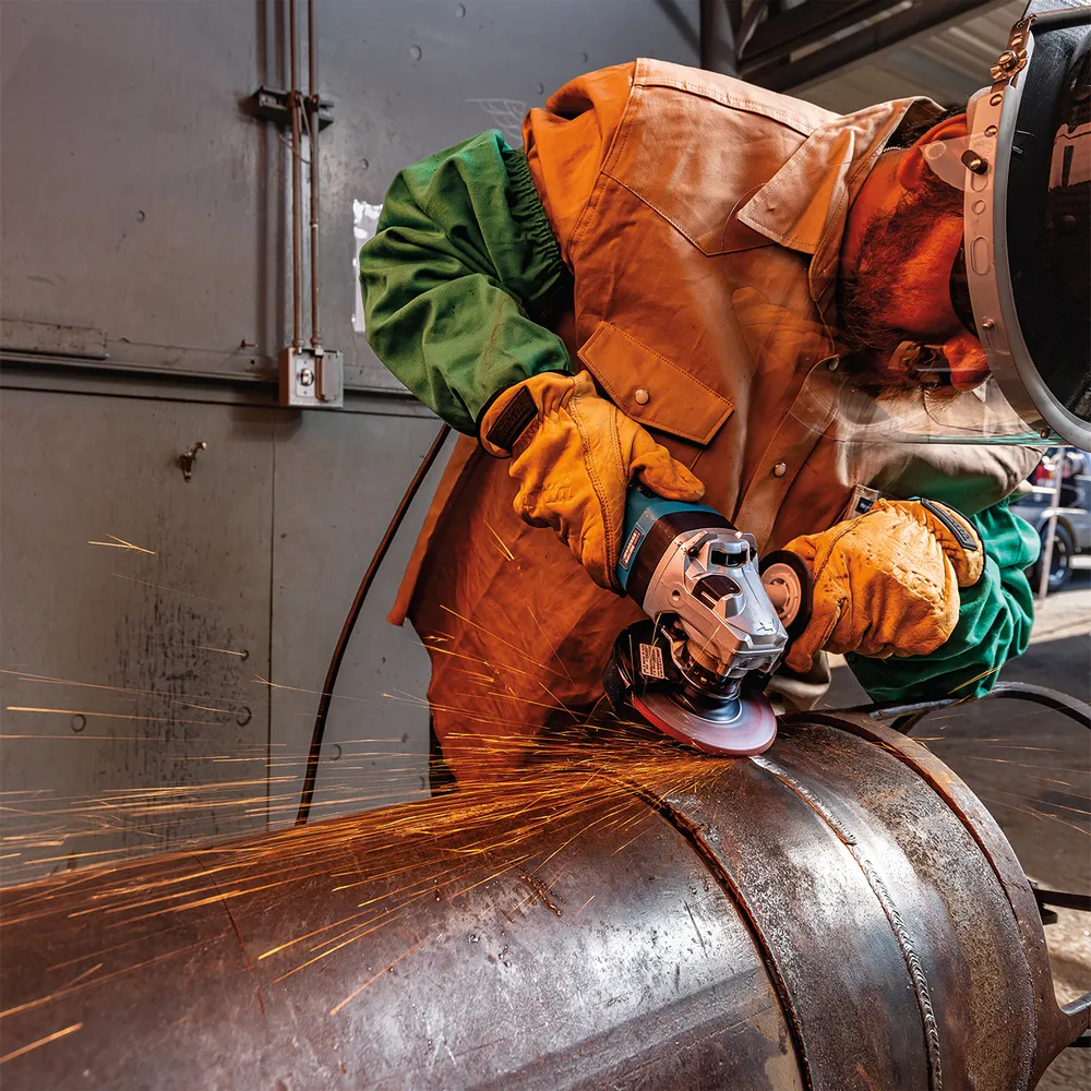 Pildil näeb Makita nurklihvija GA5091X01 kasutamist, millega töötleb metalltoru ja genereerib sädemeid.
