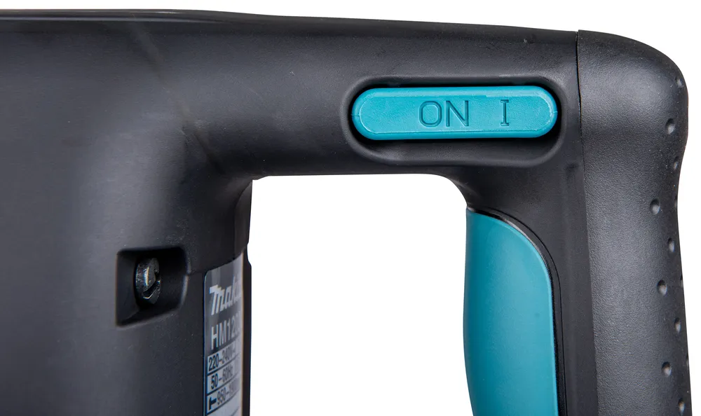 Pildil on detail Makita piikvasarast HM1203C, nähtav on masina korpus, toitelüliti ja käepide.
