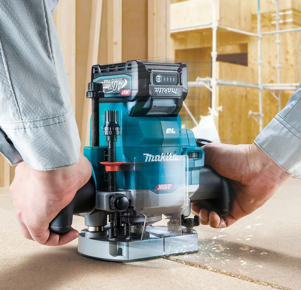 Pildil on Makita akufrees RP001GZ02 koos 40V aku ja tolmuimeja voolikuga, mis on paigutatud puidust töölauale.