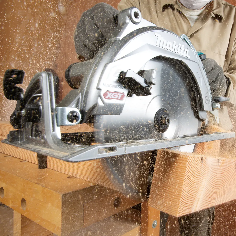 Pildil on Makita akuketassaag RS002GZ, mis lõikab puidutükki, tekitades puidulaaste.