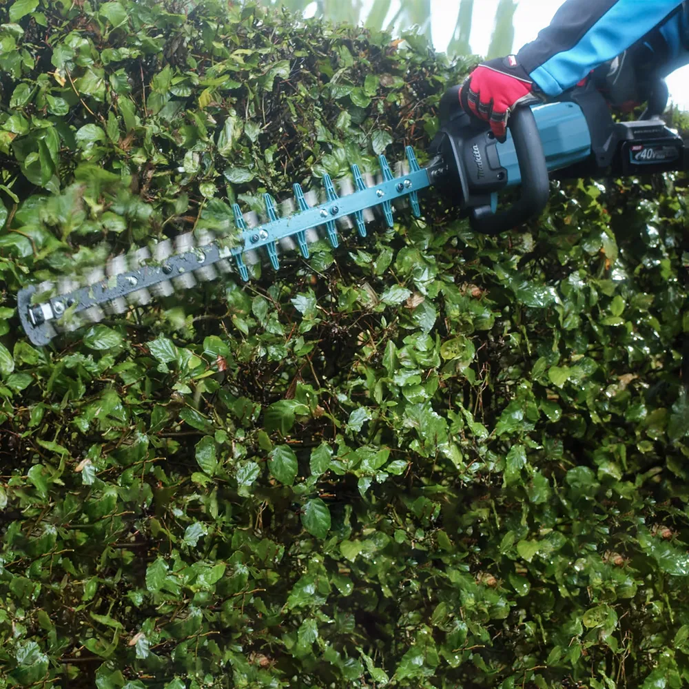 Pildil on Makita akuhekilõikur UH004GZ XGT, mis lõikab rohelise heki oksi.