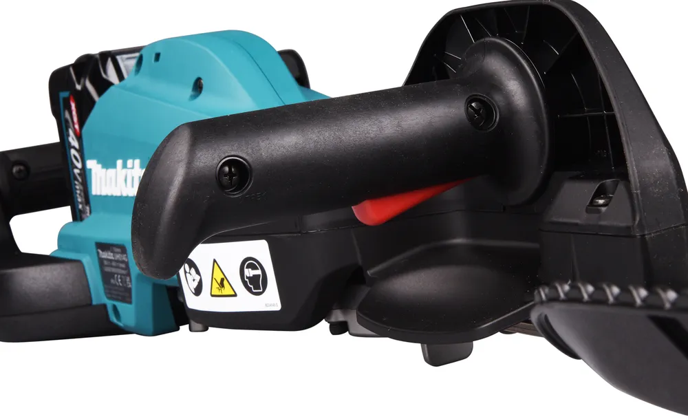 Pildil on detailne vaade Makita akuhekilõikurist UH014GZ XGT, näidates seadme käepidet, punast ohutusnuppu ja Makita logo.