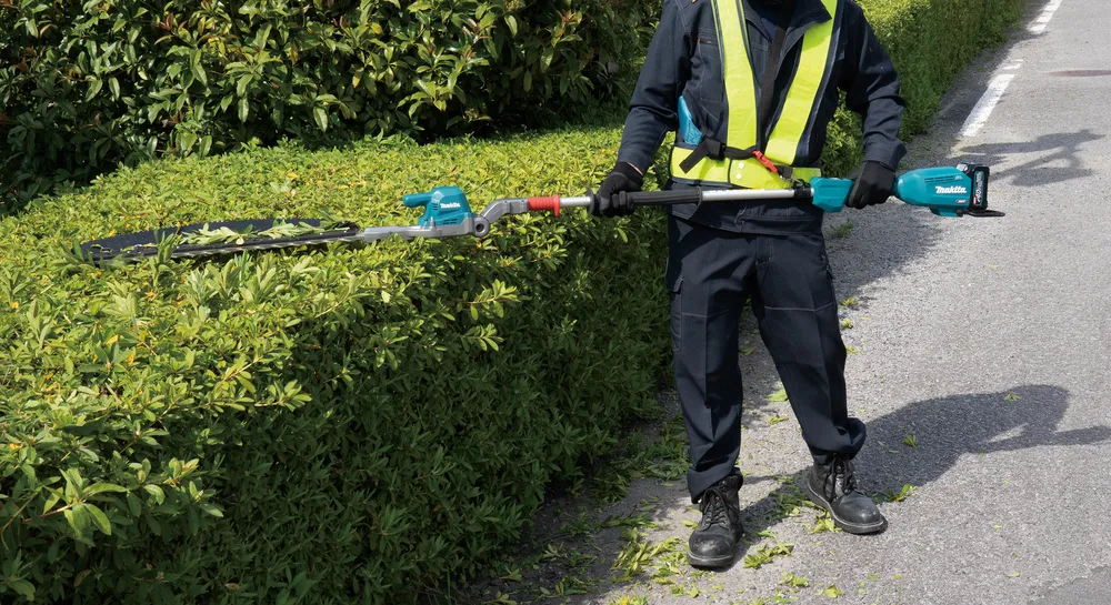 Pildil näeb meest, kes kasutab Makita akuhekilõikurit UN001GZ XGT, et heki oksi kärpida.