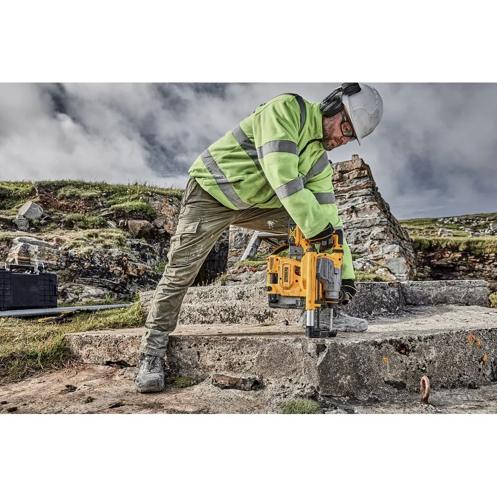 Pildil on mees tööd tegemas kollase Dewalt SDS Plus tolmueemaldussüsteemi D25304DH ja rohelise helkurvestiga.